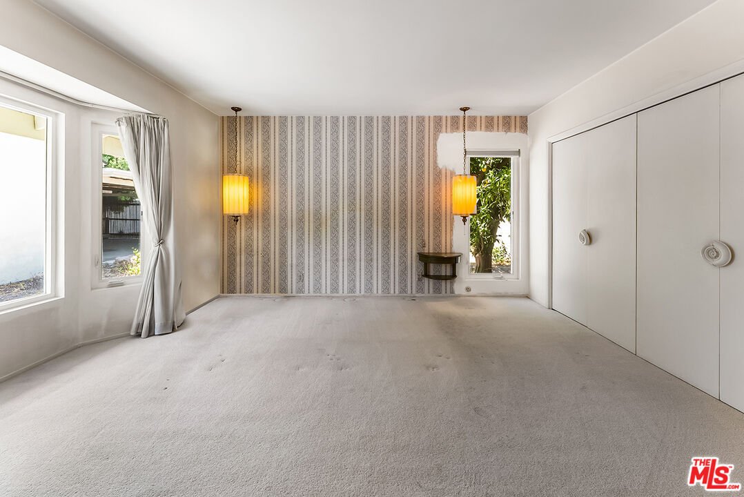Empty room with beige carpet, wallpaper, and large windows.