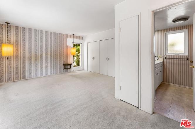 Empty room with beige carpet, striped wallpaper, and pendant lights.