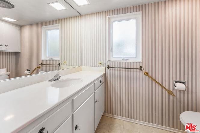 Bathroom with white countertop, striped wallpaper, and gold fixtures.
