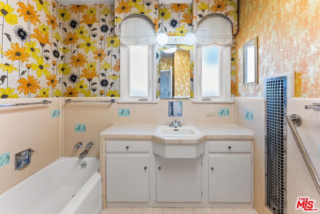 Bathroom with floral wallpaper, white bathtub, and sink with storage.