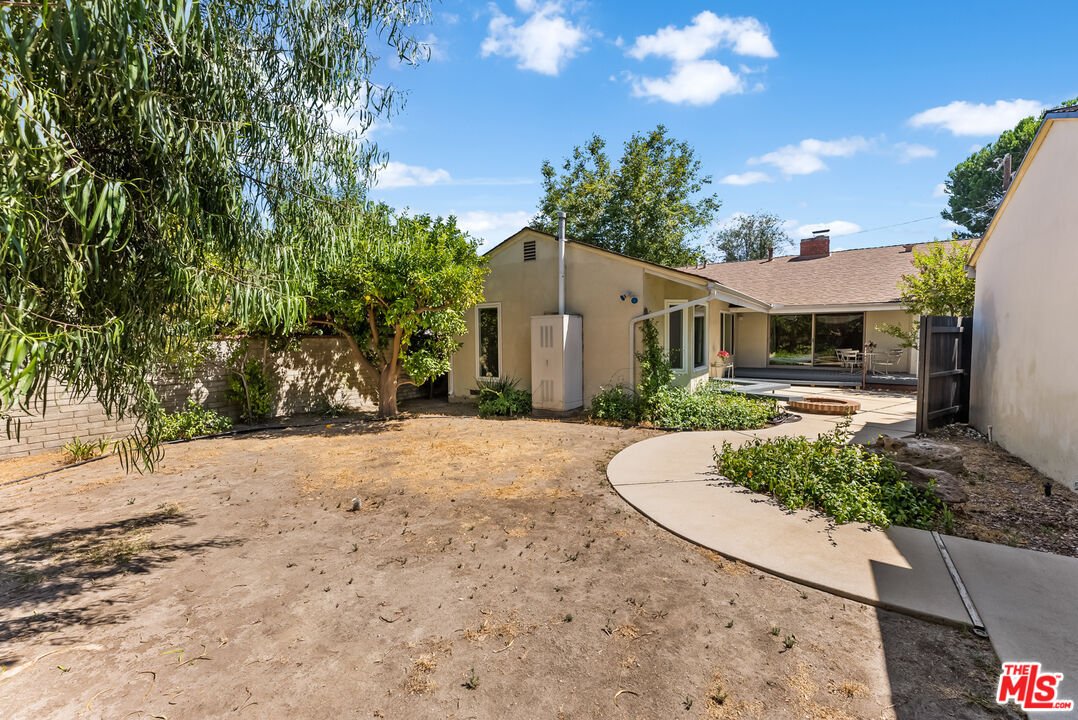 Back of house with trees, dry yard, and concrete path.