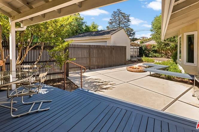 Backyard patio with wooden deck, glass table, and fire pit.