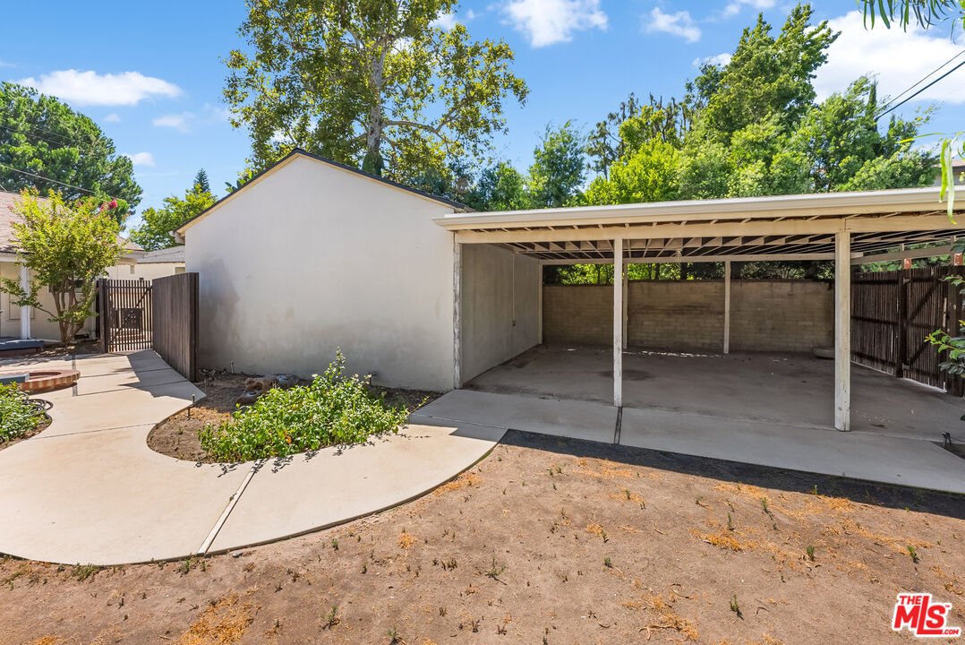Backyard with concrete area, carport, and trees.