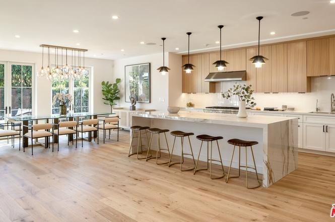 Modern kitchen with light wood cabinets, large island with bar stools, pendant lights, and open dining area with big window.