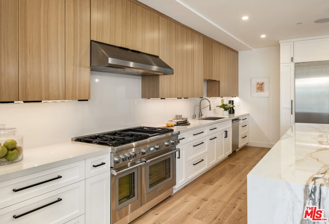 Modern kitchen with wood cabinets, gas stove, white counters, and stainless range hood in a spacious home interior.