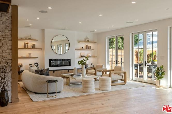 Living room with curved white sofa, round coffee table, wall-mounted fireplace, shelves with decor, and glass doors to patio