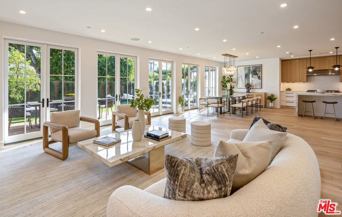 Living room with soft seats, coffee table, big glass doors to patio, and dining area behind.