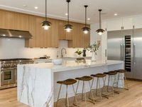 Kitchen with light wood cabinets, marble countertop, pendant lights, island with seating, and stainless steel appliances