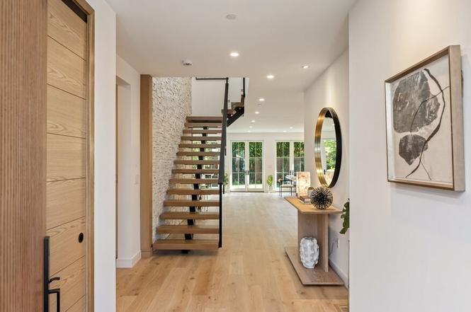 Entryway with wooden door, staircase with metal railing, large windows, abstract painting, console table, and light wood floor