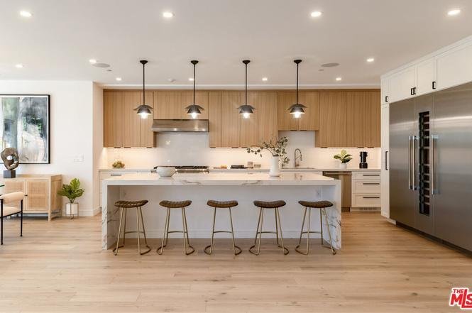 Kitchen with large island, bar stools, wood cabinets, pendant lights, and stainless steel appliances.