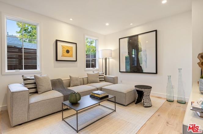 Living room with light sofa, pillows, coffee table, and two windows with natural light.