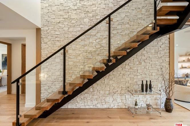 Stairs with wood steps, black metal railing, and stone wall feature.