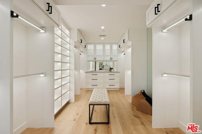 Walk-in closet with white cabinets, lighted shelves, center bench, and wood floor.