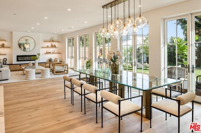 Dining area with glass table, chairs, and big windows with natural light.