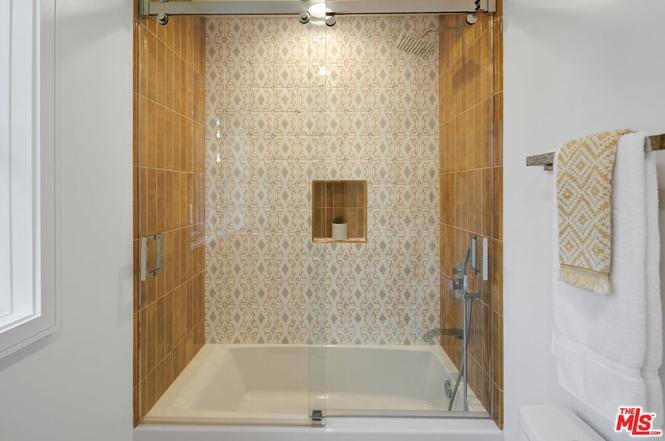 Bathroom with bathtub, glass sliding door, tiled wall, and small shelf for toiletries.
