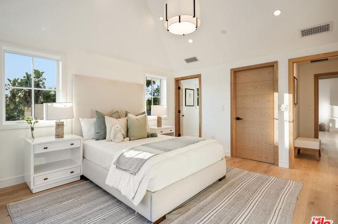 Bedroom with white bed, soft bedding, bedside lamps, light rug, big windows, and ceiling light.