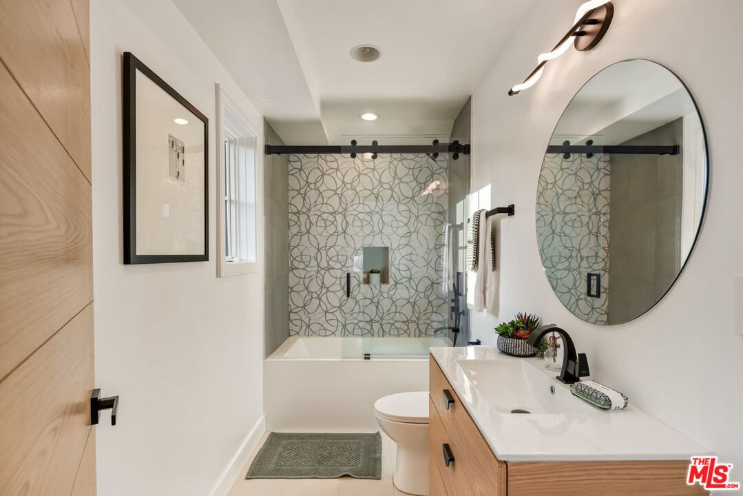 Bathroom with bathtub, patterned glass shower door, round mirror, and vanity with storage.