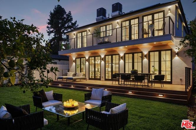 Backyard with dining table, chairs, lawn, lounge seats with cushions, and green plants.