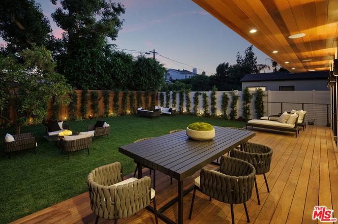 Two story house with big windows, green plants, and outdoor seating in front California real estate.