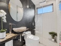 Bathroom with round mirror, stone sink, glass-door shower, and plants