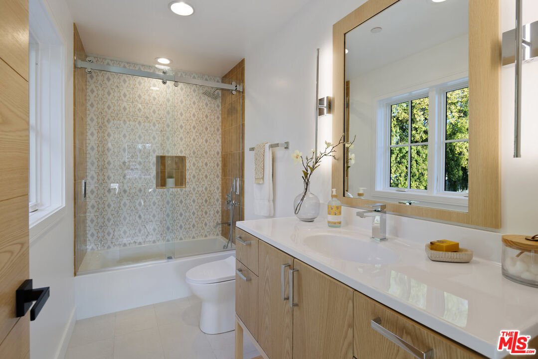 Bathroom with glass shower, wood cabinets, white counter, and big windows.