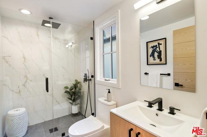 Bathroom with glass shower, marble walls, wall mirror, small plant, and simple fixtures.
