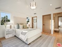 Bedroom with bed, light bedding, decorative pillows, nightstand with lamp, windows, and wooden floor with rug