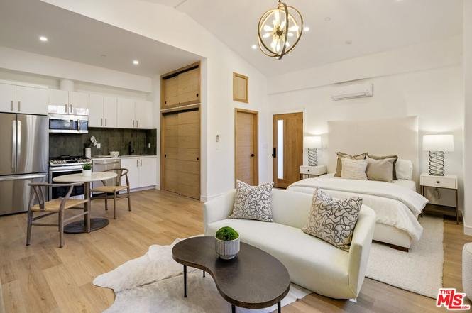 Small studio apartment with bed, sofa, dining table, kitchen appliances, and wood floor.