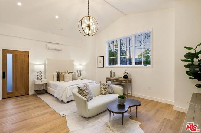 Bedroom with bed, pillows, armchair with small table, stylish lights, and big window.