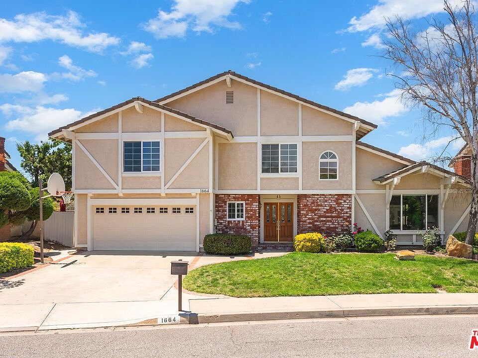 Two story house with tan exterior, brick accents, front yard, driveway, garage, and big windows California real estate.