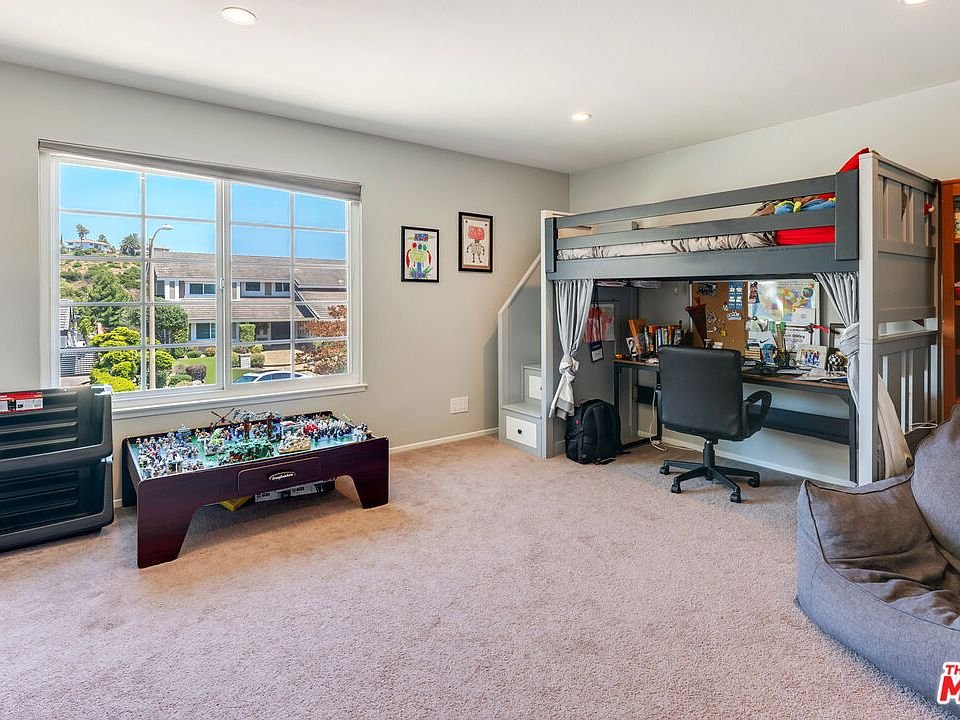 Bedroom with loft bunk bed, desk below, bean bag chair, game table, window, and soft carpet.
