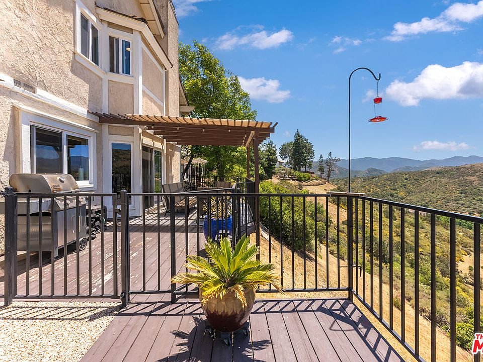 Balcony with grill and bird feeder overlooking hills.