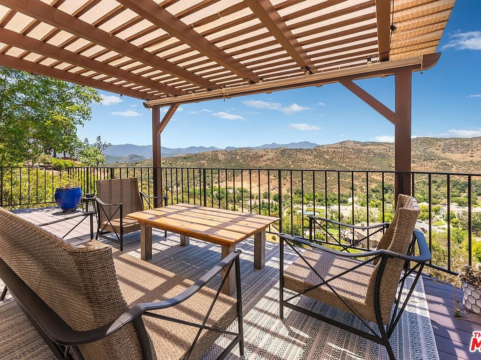 Patio with wood table, chairs, pergola, and hill view California real estate.