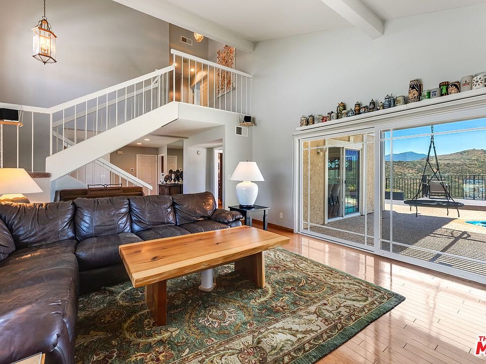Living room with leather sectional sofa, wood coffee table, big windows with outdoor view, stairs, and shelf decor.