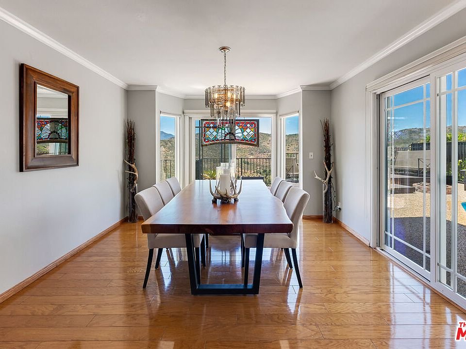 Dining room with wood table, white chairs, chandelier, and big windows.
