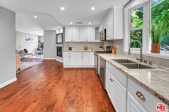 Kitchen with wood floor, white cabinets, stainless steel appliances, and window above sink.
