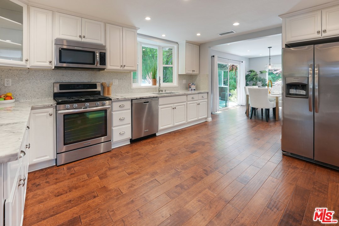 Kitchen with white cabinets, stainless steel appliances, wood floor, window, and dining area.