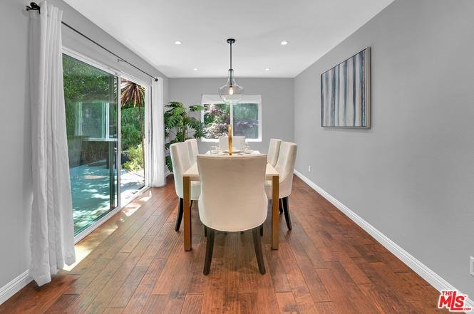 Dining room with wooden table, white chairs, large windows, and garden view.