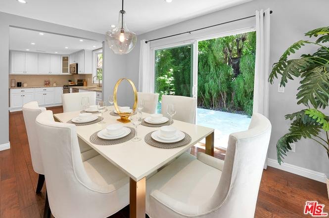 Dining room with white table, six chairs, centerpiece, sliding glass doors, and garden view.