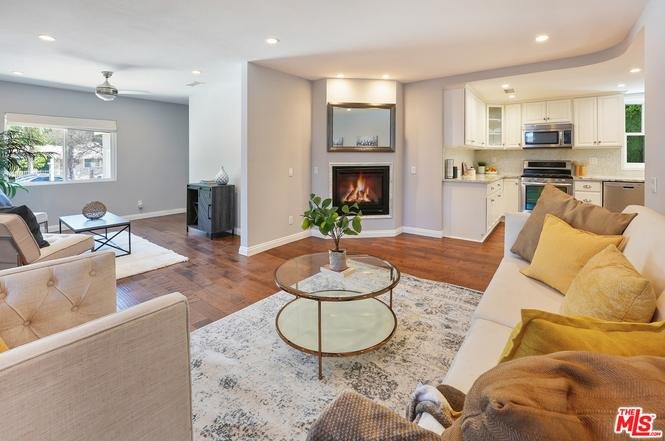 Living room with sectional sofa, pillows, glass coffee table, plant, fireplace, and large windows.