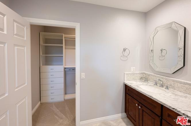 Bathroom with double sinks, dark wood cabinets, mirror, door to closet, gray walls, and tile floor.