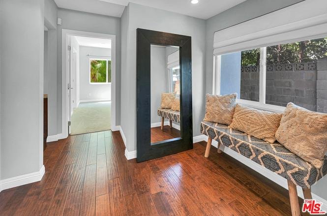 Hallway with large mirror, bench with pillows, and windows.