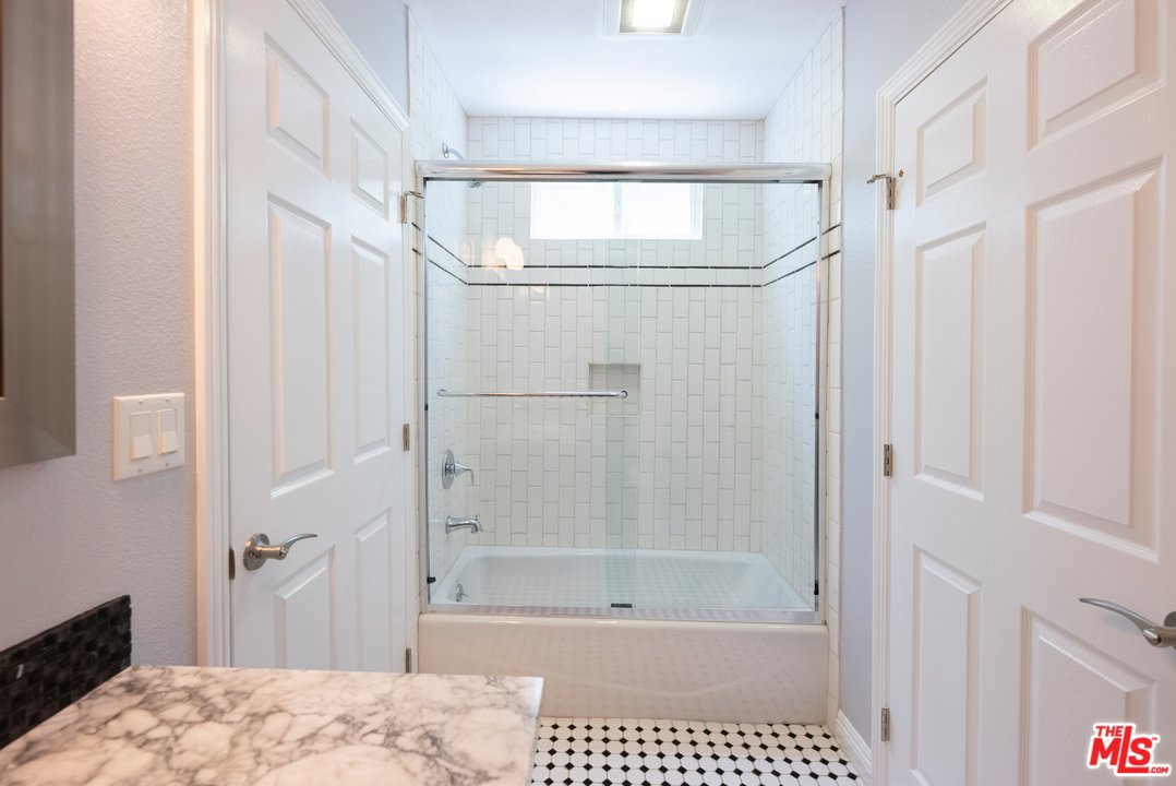 Bathroom with glass shower, bath tub, white tiles, and dark marble counter