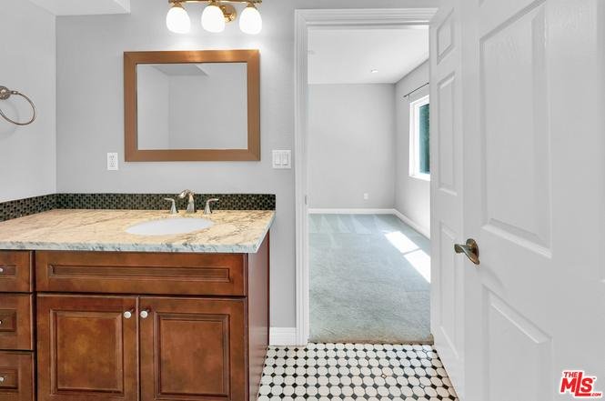 Bathroom with dark wood cabinets, counter, mirror, and open doorway to another room.