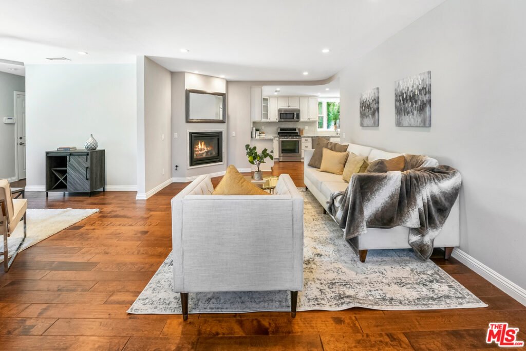 Living room with white sofa, pillows, fireplace, wood floor, gray rug, and wall art.