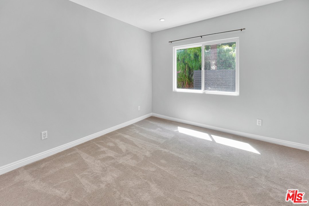 Empty room with light gray walls, a window with a view of greenery, and beige carpet.