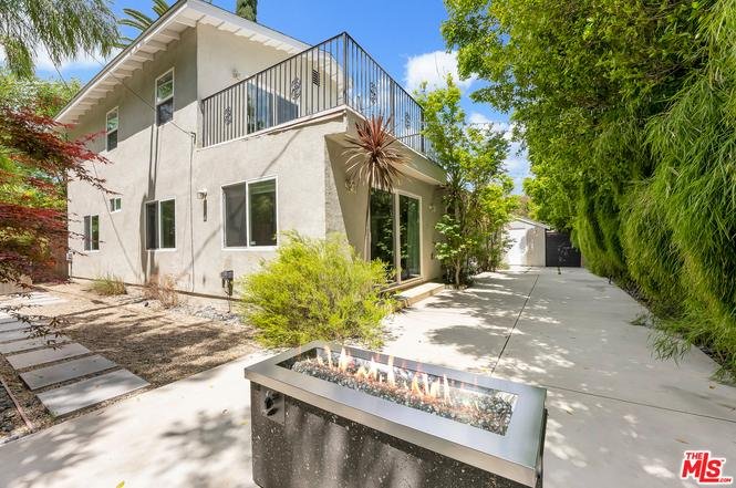 California real estate house with white exterior, balcony, patio fire pit, pathway, and trees.