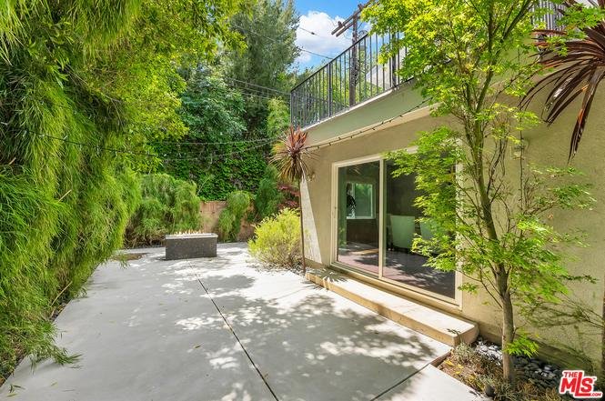 Patio with concrete floor, trees, plants, and building with large windows.