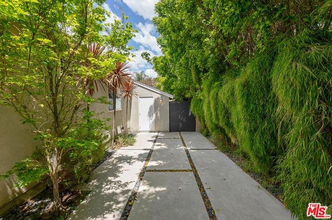 Walkway to black gate with trees and green plants.