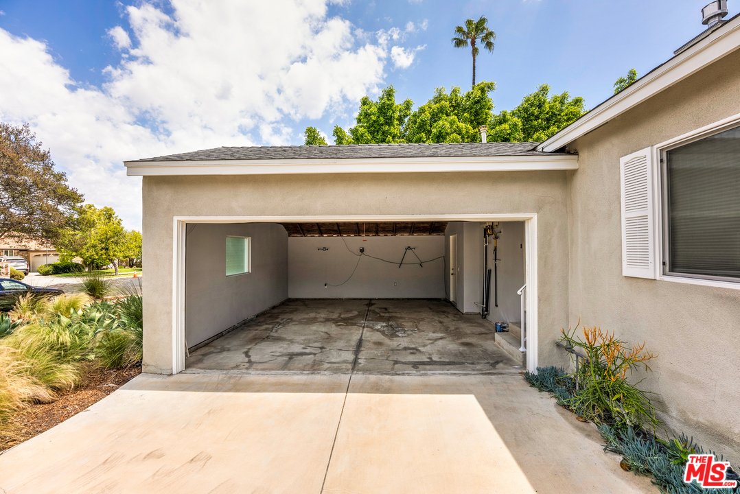 Residential garage with empty space, concrete floor, and palm trees outside.